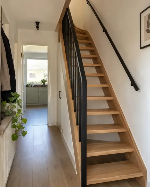Open eiken trap met eenvoudige zwarte balustrade in een Nederlandse jaren 70 woning